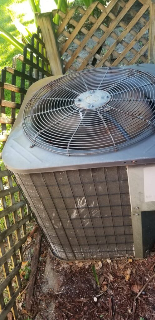Outdoor residential air-conditioning condenser beside a wood fence