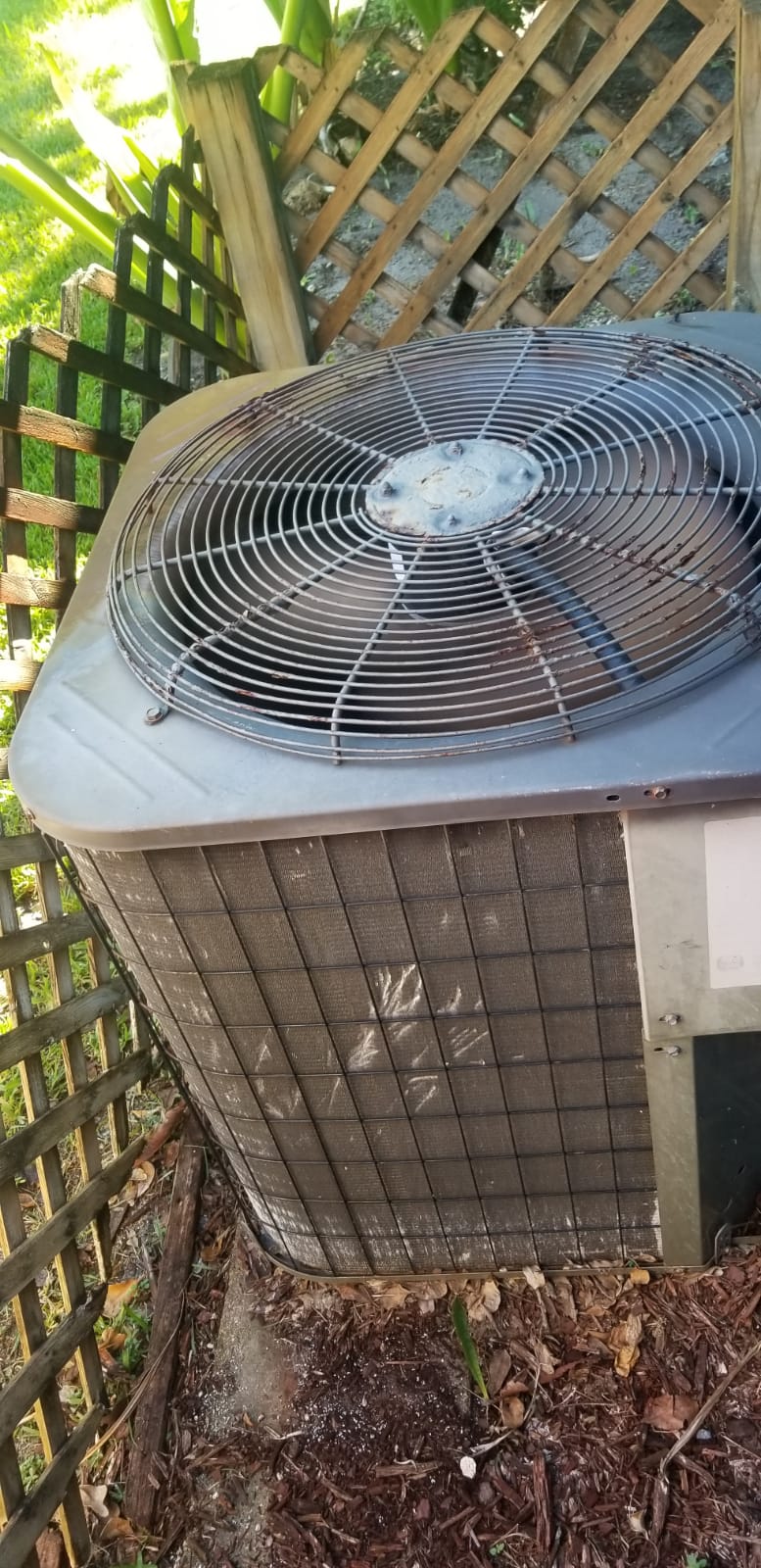 Outdoor residential air-conditioning condenser beside a wood fence